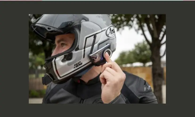 This photo features a guy with his mototcycle helmet on. He is pointing to or using the device in this giveaway. There are also green trees in the background as if to show an outdoor adventure ready to ride into.