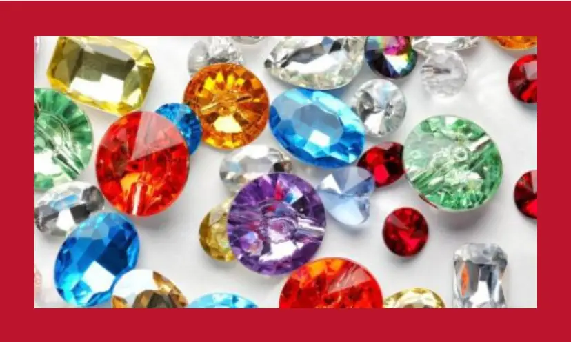 This photo shows an array of colorful gems and stones that could make a gorgeous peace of jewelry. There are reds, blues, golds, purple, clear and more, creating a rainbow of sparkle.