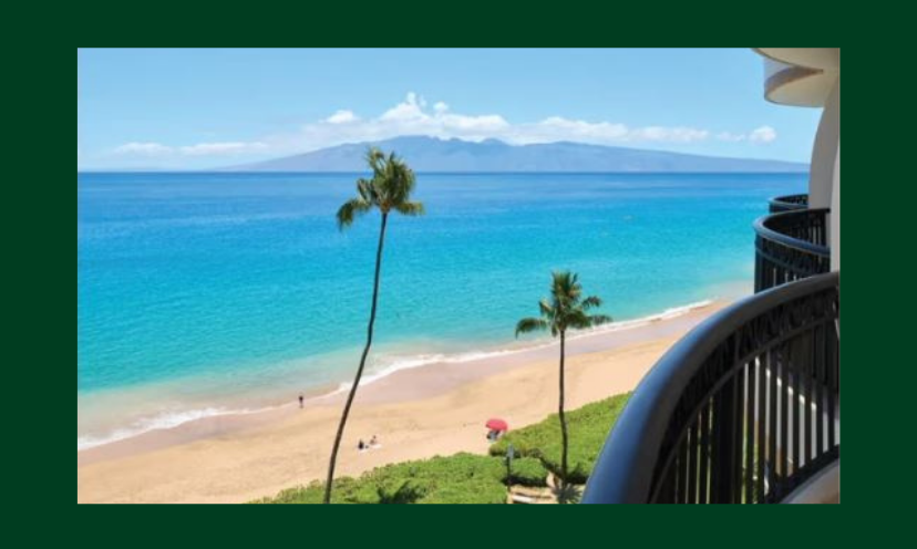 This is one of many photos that shows the beauty and appeal of Maui Hawaii. It appears to be a shot taken from a hotel balcony complete with crystal clear water, a sandy beach, palm trees and mountains far in the background!