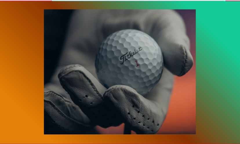 This is a close up photo of a golfers hand, complete with glove, holding a Titleist golf ball.