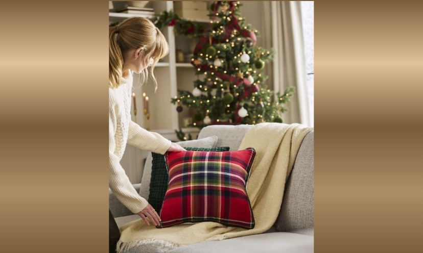 This photo shows a younger woman decorating her home for the holidays with a festive pillow on a new couch and a sparkling Christmas tree in the background!