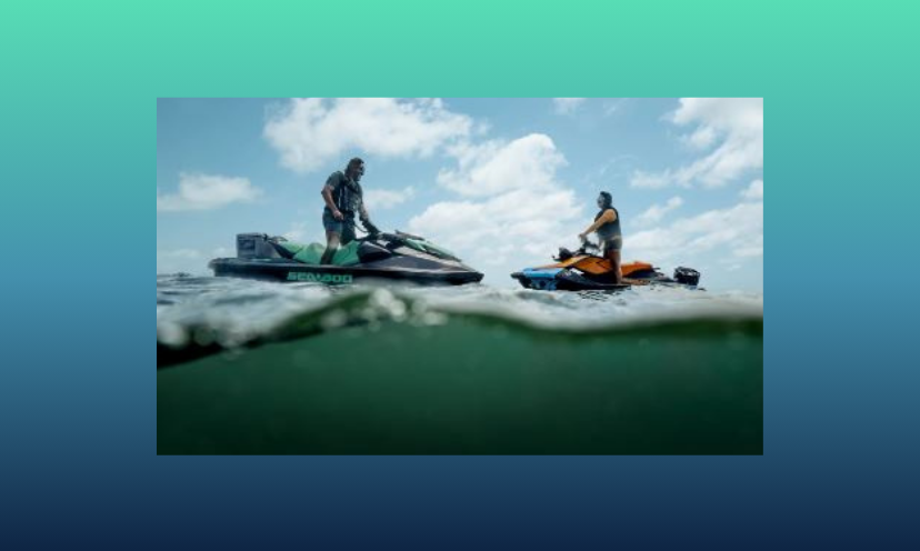 This is a photo of two people both on a SeaDoo watercraft, riding the glistening, aqua colored ocean waves!