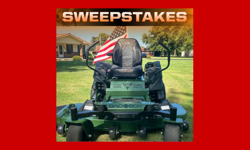 This photo features the Bad Boy Military edition zero turn lawn mower offered in this sweepstakes. It is sitting in front of a home on a beautiful lawn with the USA flag waving behind it!